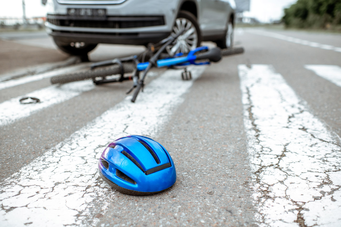 Bicycle accident scene with a helmet on the ground and a bicycle under a car in the background