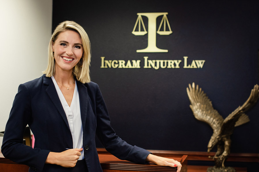 Attorney Megan E. Ingram posing at the office front desk with the Ingram Injury Law logo in the background