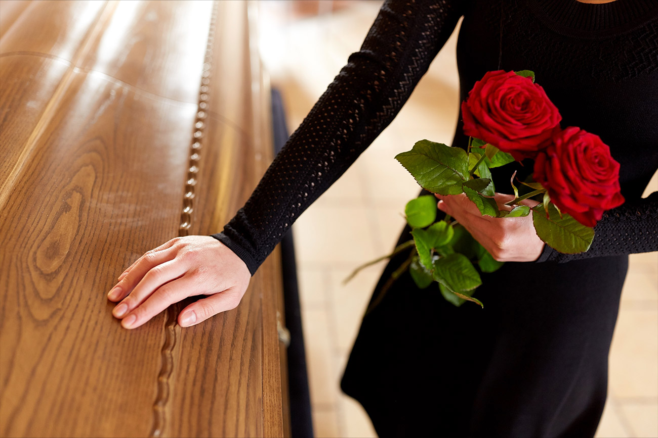 A woman holding roses & placing her hand on a coffin